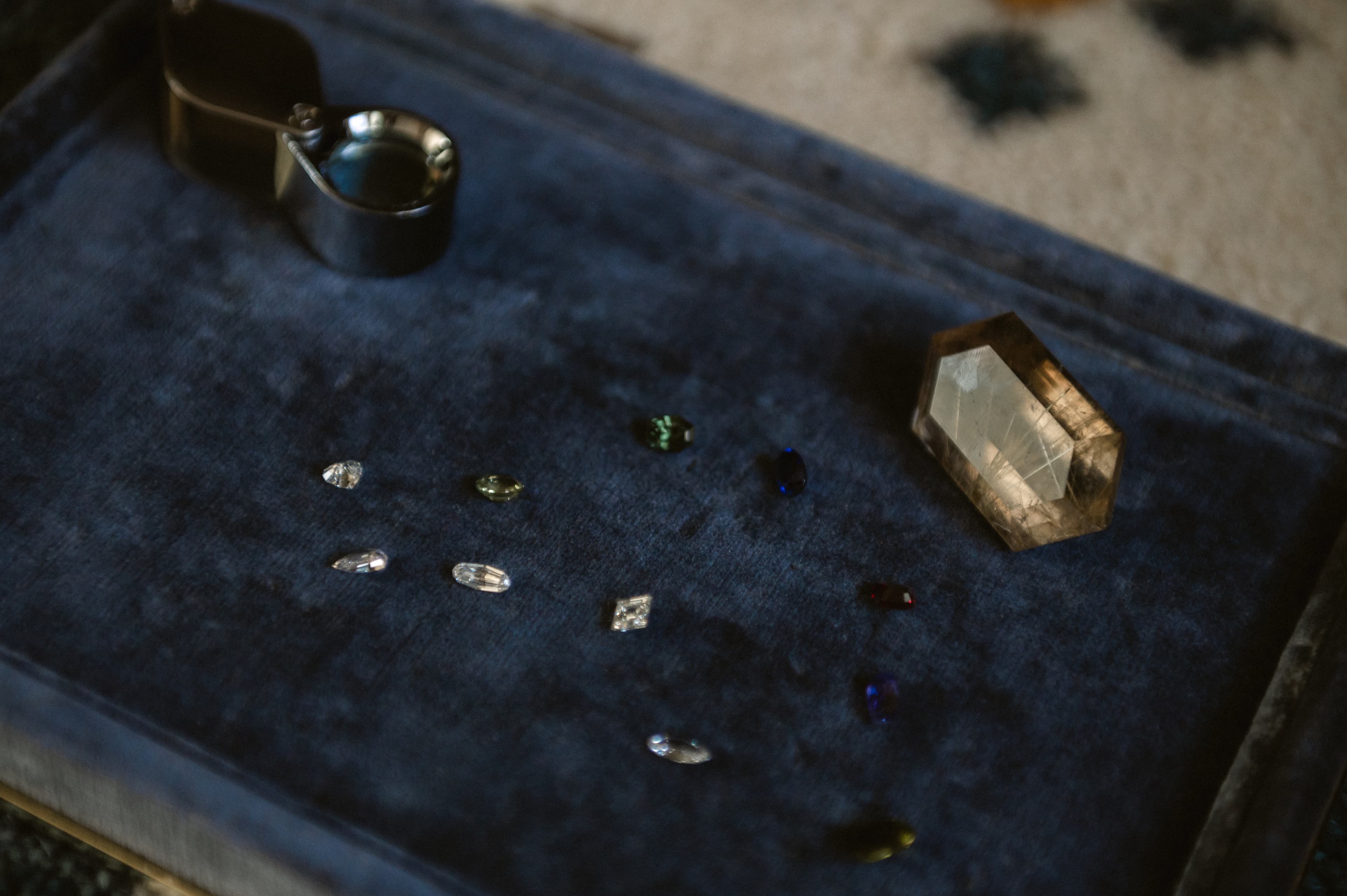 Loose gemstones and a rough citrine arranged on a navy velvet jeweler's tray